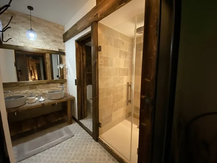 Salle de bains en bois et pierre avec porte de douche en verre clair et miroir encadré de bois
