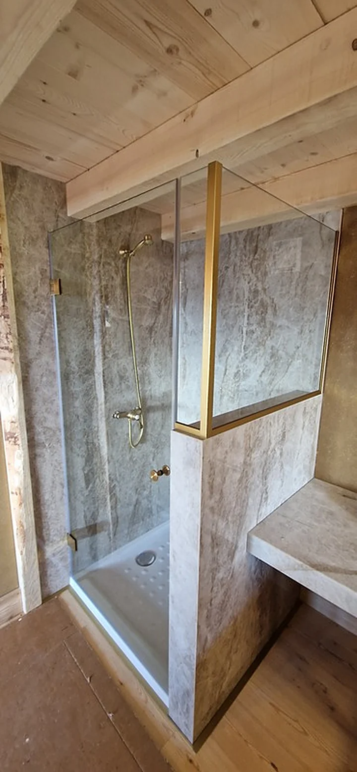 Paroi de douche avec profils en laiton brossé, sous un plafond en bois